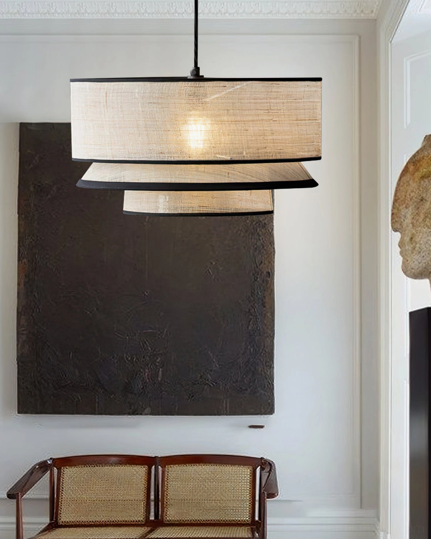 Fabric layered pendant light hanging above minimalist lounge corner with vintage rattan bench and dark abstract wall art