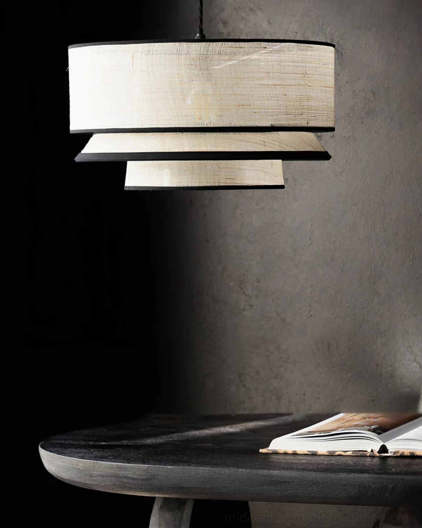 Dark accent corner interior with layered fabric pendant light above small black round table and open book styling