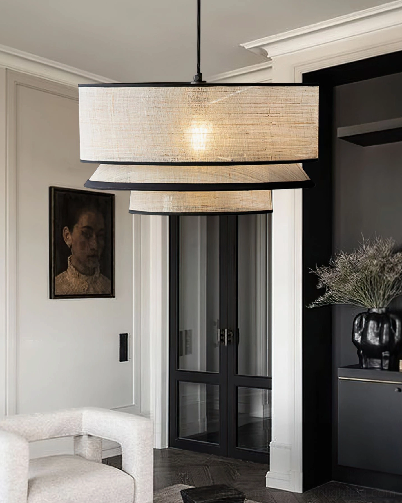 Two-tiered drum pendant light in residential entryway hallway with white accent chair and portrait wall decoration