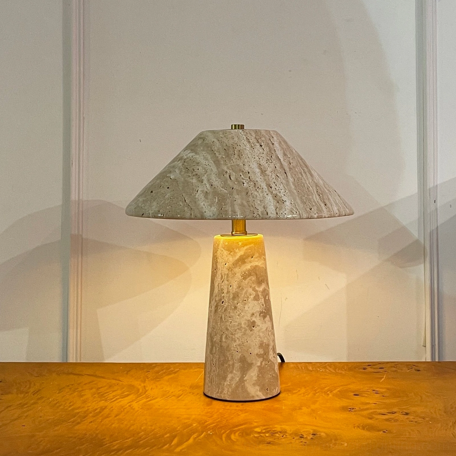 Lydia travertine table lamp three-quarter lit view warm glow with brass hardware detail on wood surface