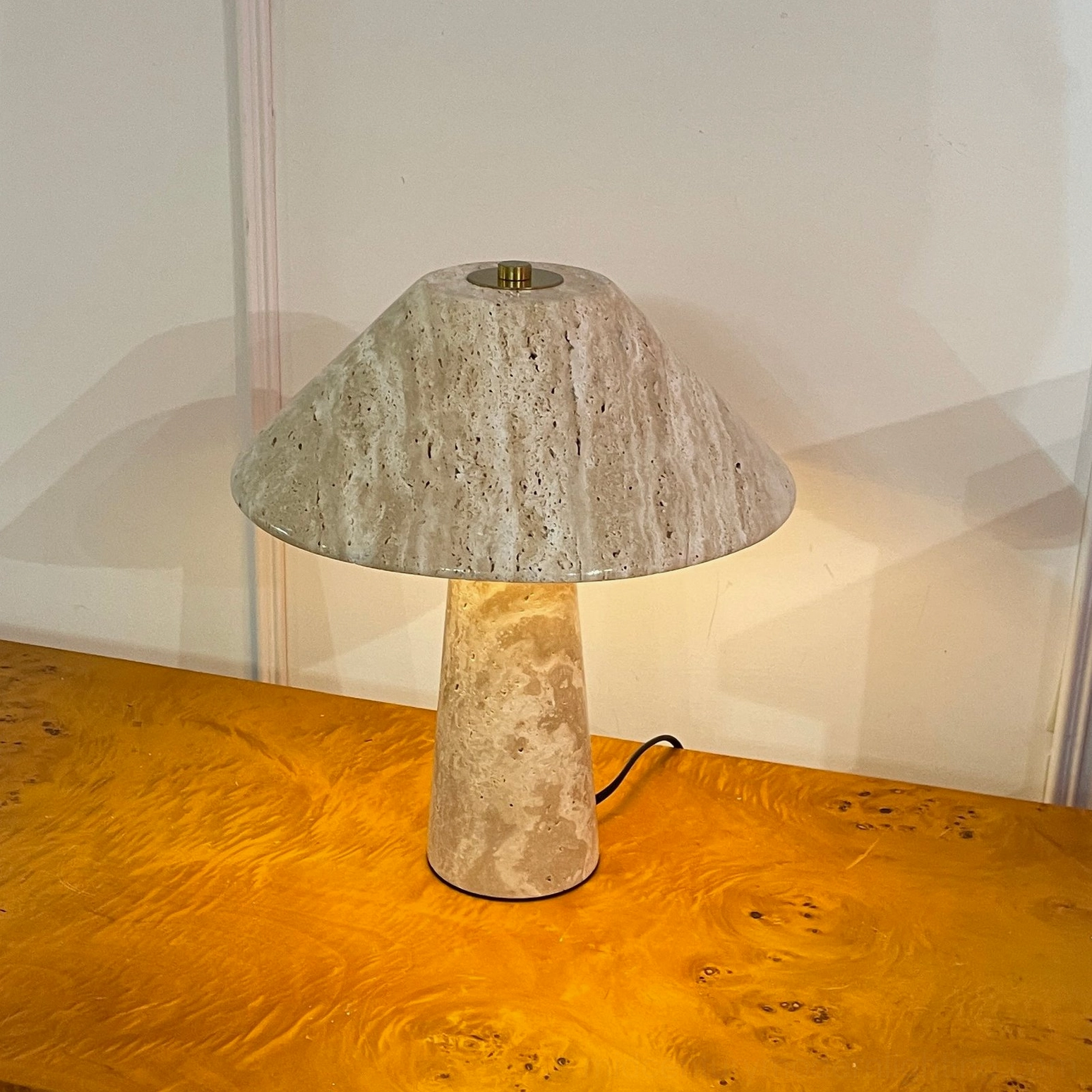 Lydia travertine table lamp three-quarter view illuminated on burl wood console showing warm ambient glow
