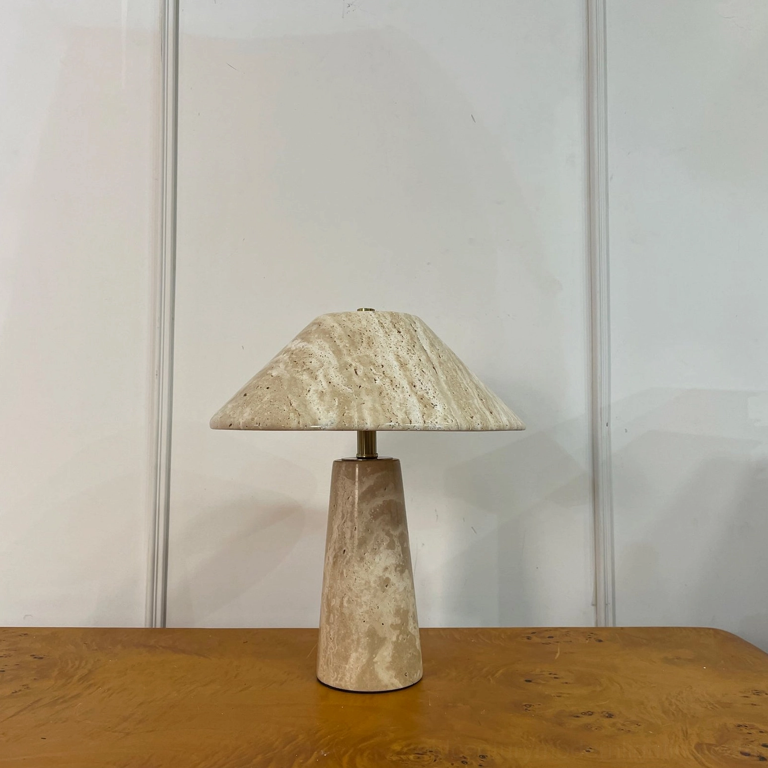 Lydia tapered travertine lamp side front view on wood table with paneled white wall architectural backdrop