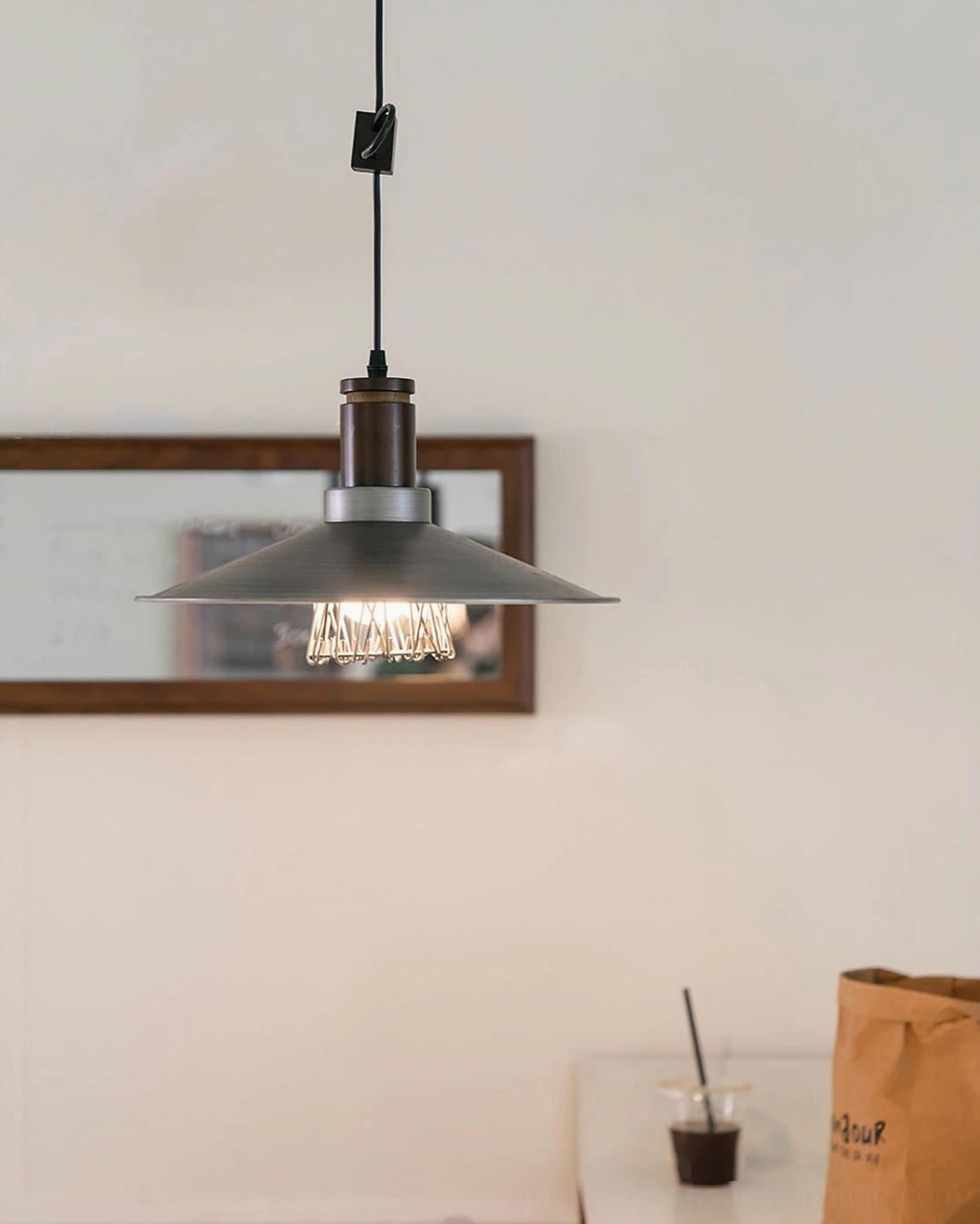 Illuminated Lyfa pendant light installed beneath wall mirror showing brushed metal finish and warm glow