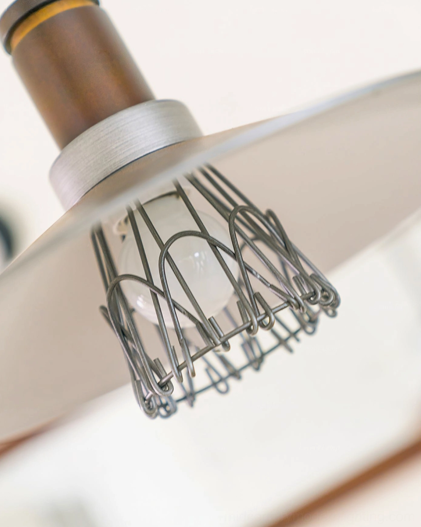 Low-angle close-up of Lyfa pendant bulb section with curved metal wire guard and brushed aluminum shade