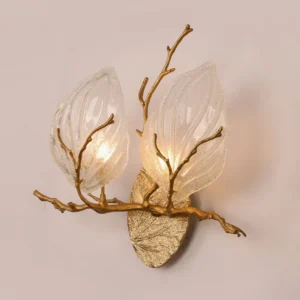 Side angle view of magnolia brass sconce showing textured frosted glass leaves with raised veins and warm glowing G9 bulbs against pale pink wall