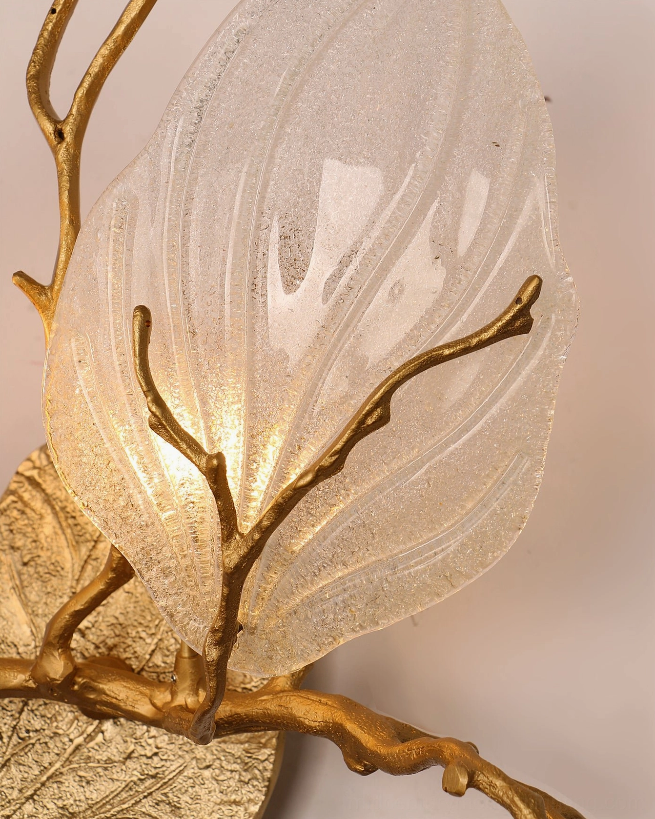 Extreme close-up macro view of magnolia brass sconce showing detailed frosted glass texture with raised veins and warm internal glow