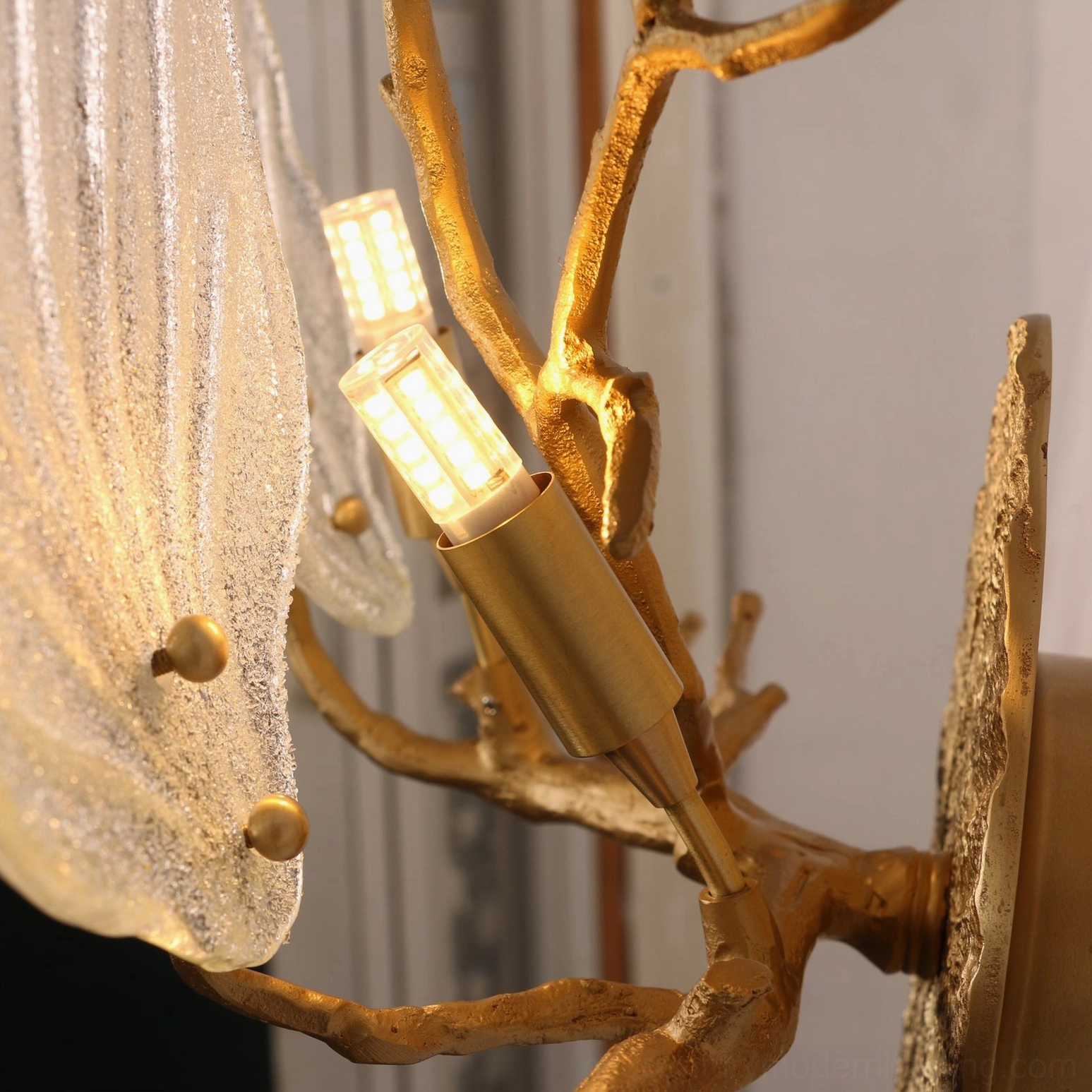 Magnolia brass sconce illuminated showing warm diffused light through frosted glass leaves in bedroom ambiance setting