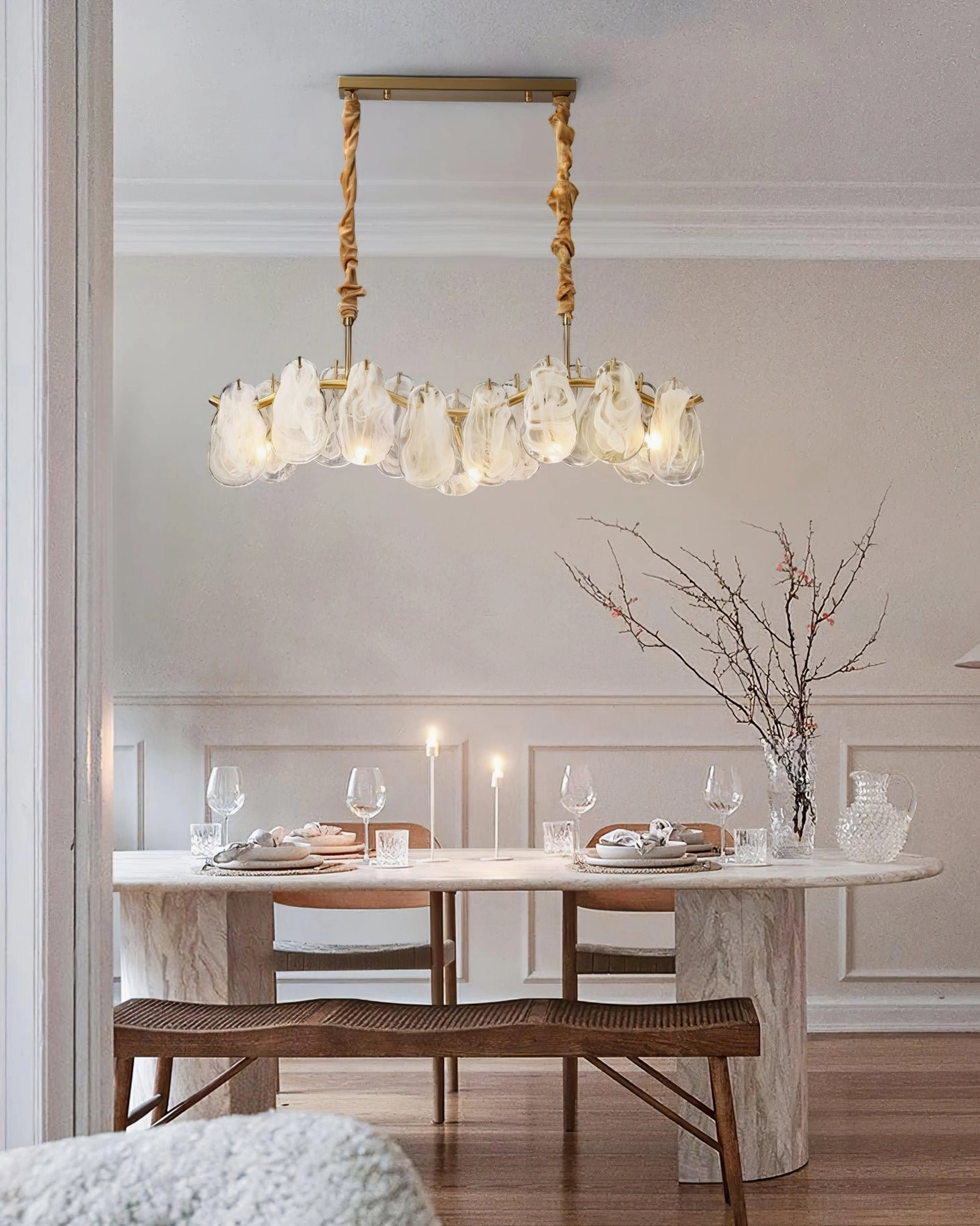 Modern sculptural glass chandelier illuminated above dining table in minimalist luxury interior with neutral color palette
