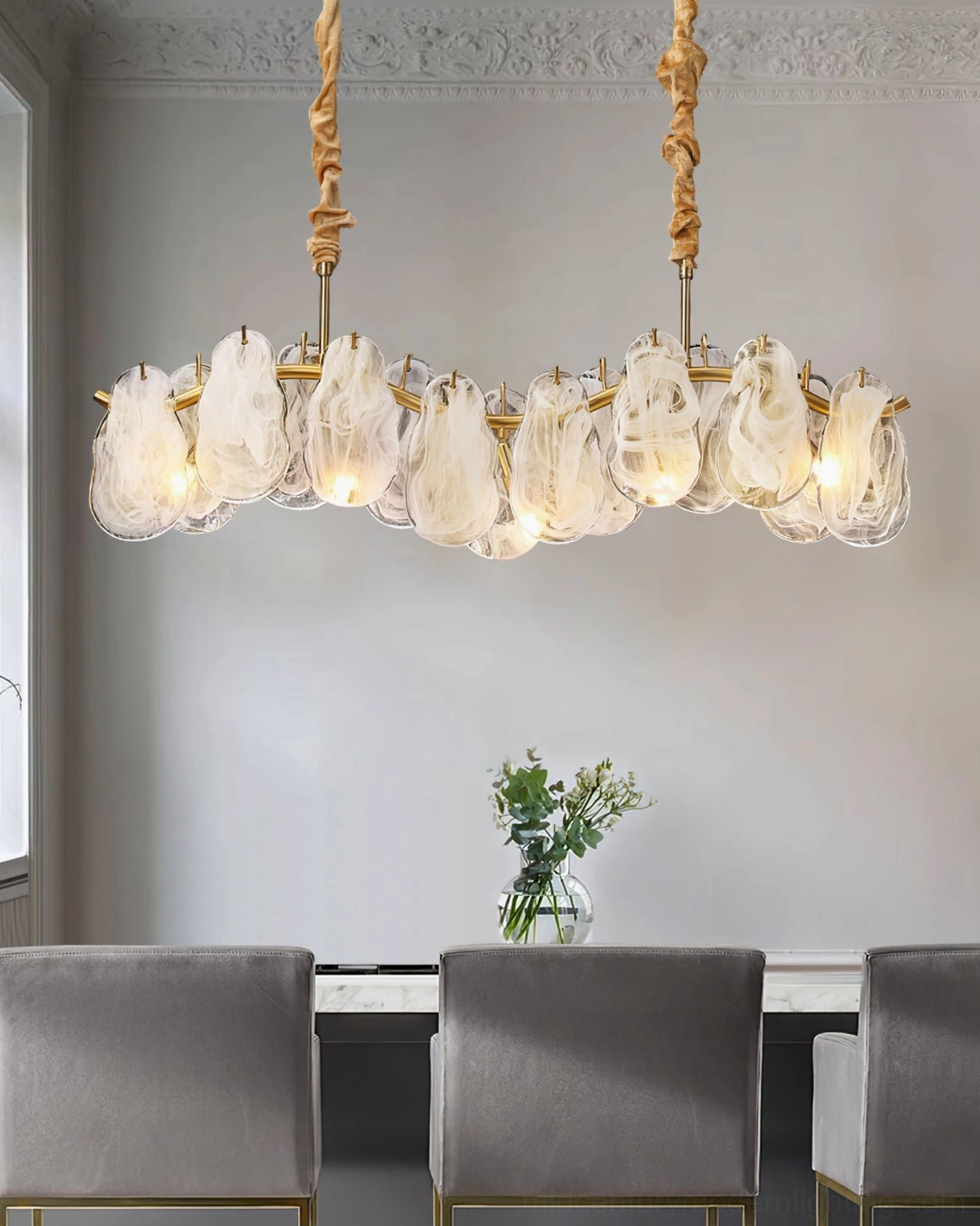 Contemporary cloud pendant light fixture in modern dining room with grey upholstered chairs and green flower arrangement tabletop styling