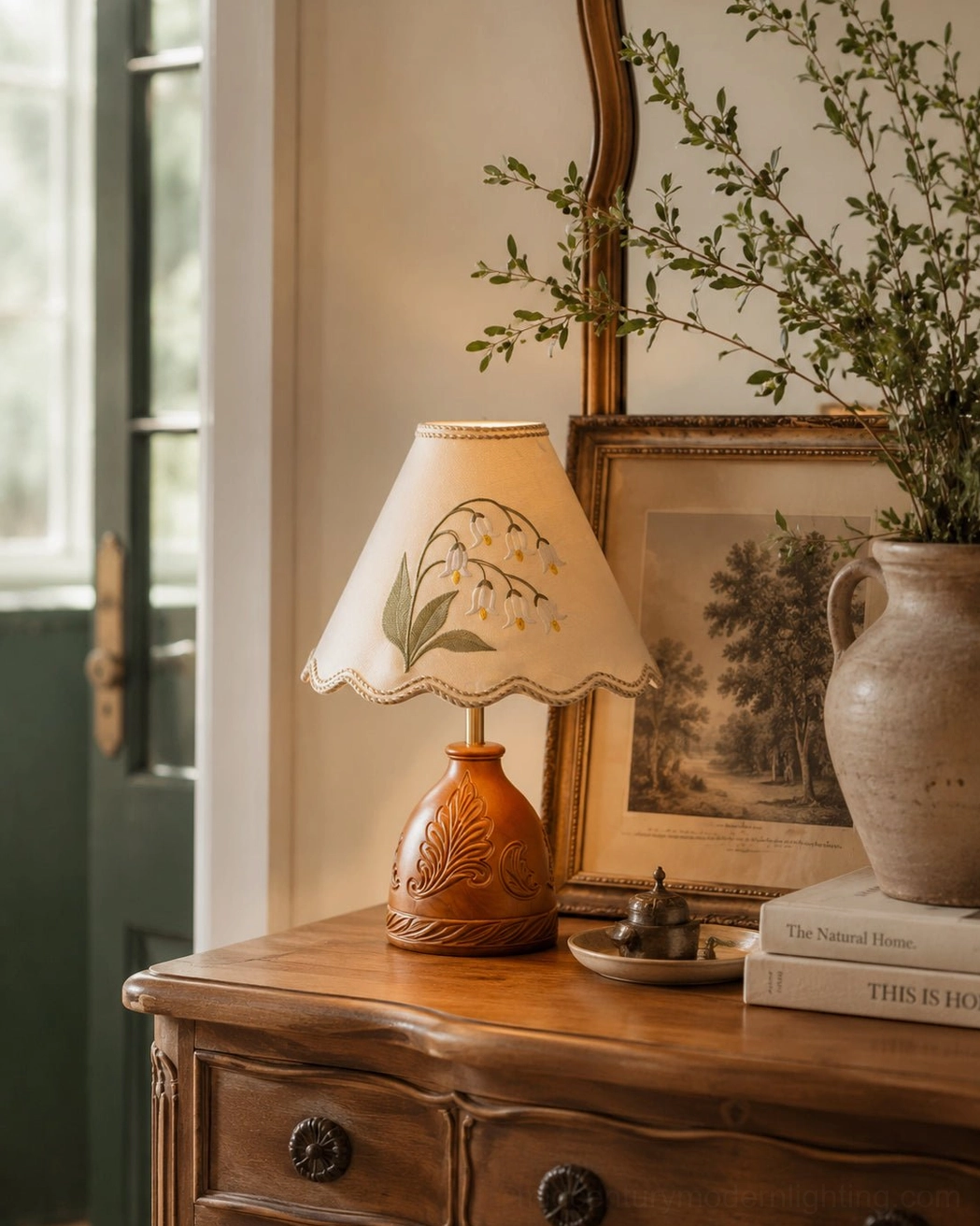 Carved wooden base lamp positioned on vintage dresser with framed painting and ceramic vase entryway display