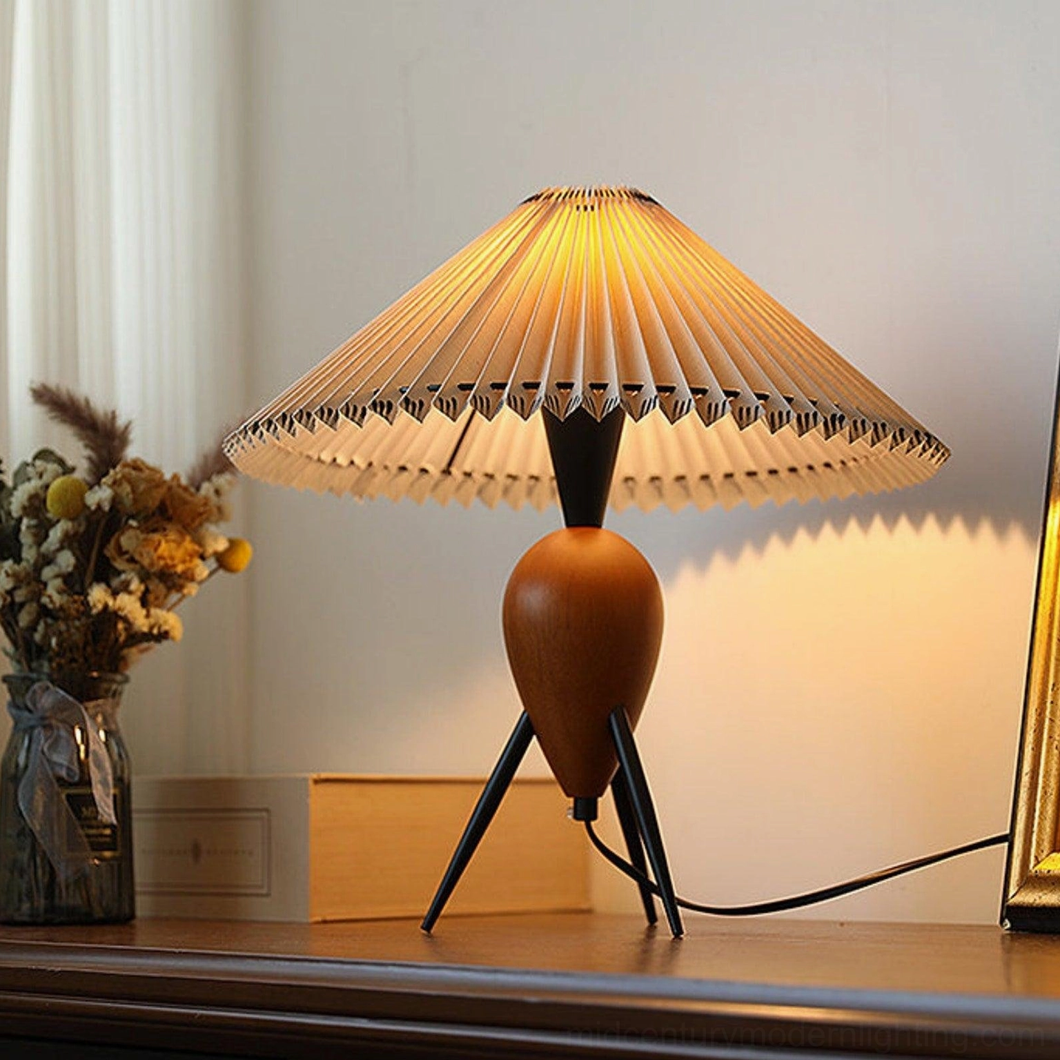 Makie tripod table lamp glowing softly on wooden cabinet with dried bouquet and golden frame mirror