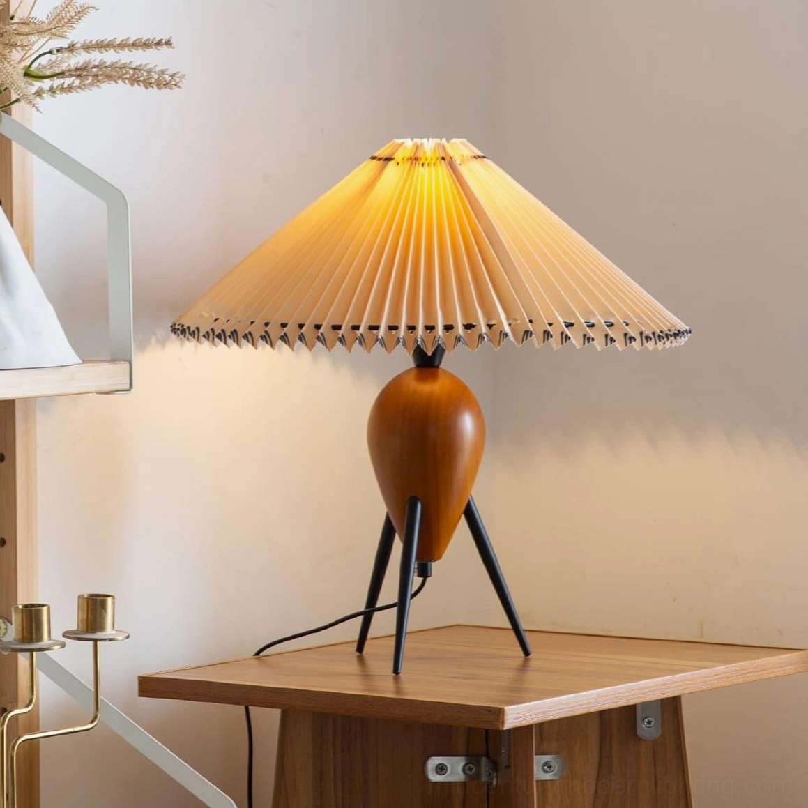 Lit Makie tripod lamp casting warm ambient light on side table, showcasing pleated shade glow in home interior