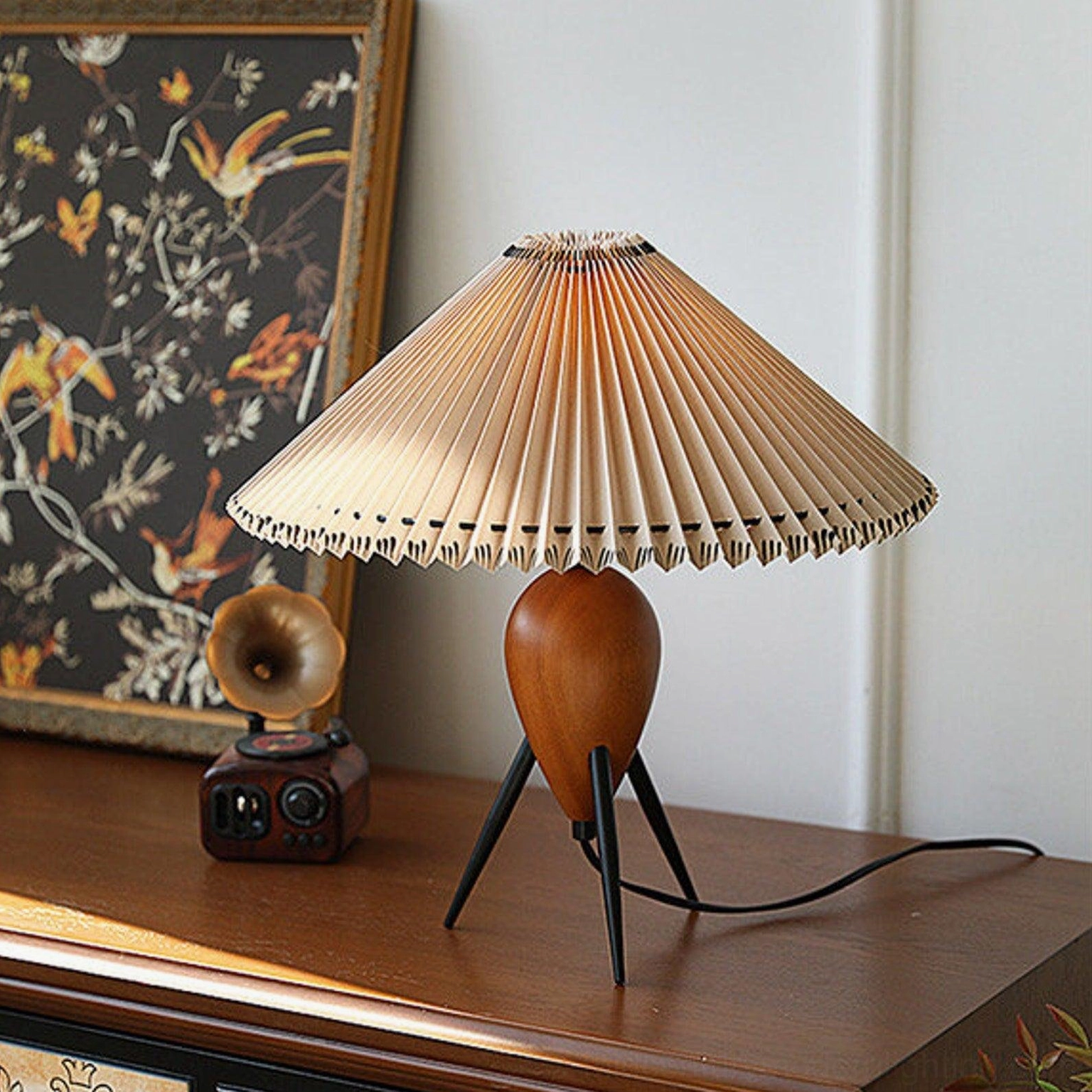 Makie tripod lamp beside vintage gramophone and floral artwork on wooden cabinet, mid-century vignette