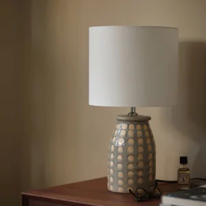 Ceramic patterned table lamp styled on wooden side table with essential oil bottle and glasses, three-quarter front view