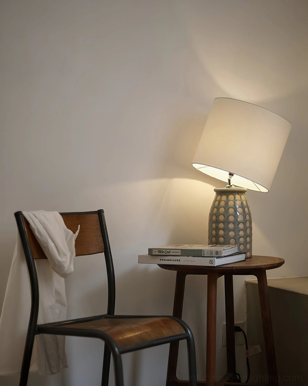 Illuminated ceramic patterned table lamp with fabric shade creating warm light, three-quarter view with white chair accent