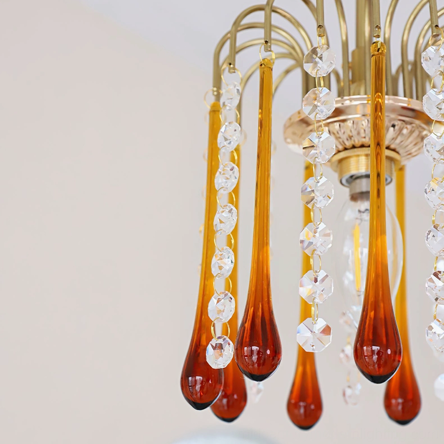 Close-up detail of Maltose brass frame and dual-tone amber and clear crystal pendant glass droplets on white background