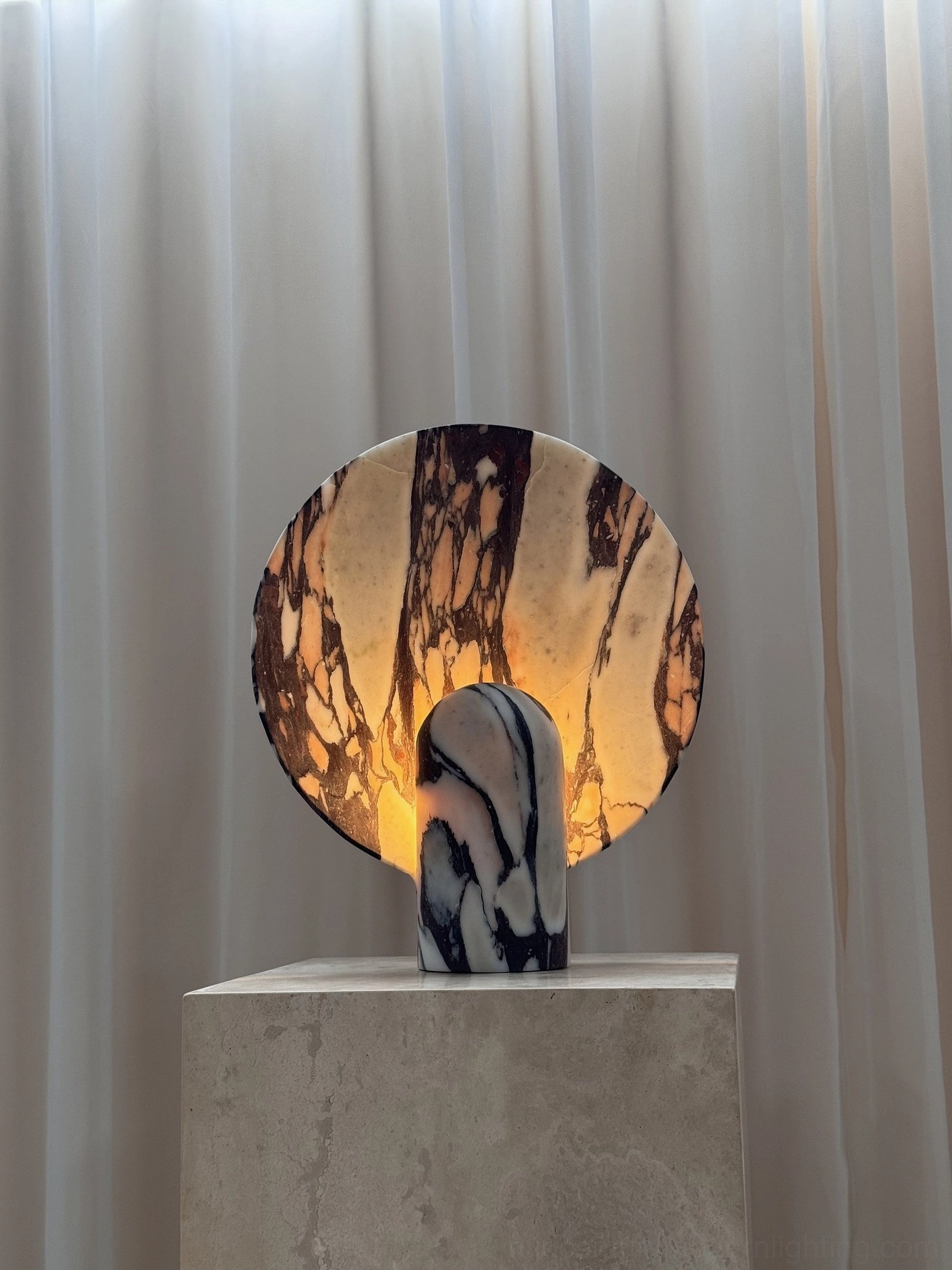 Close-up front view of purple-brown veined marble table lamp with integrated LED creating warm interior light against soft studio curtain background