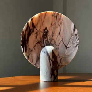 Contemporary marble table lamp illuminated on wooden table with warm ambient light showcasing rich natural marble grain texture and mid-century minimalist design