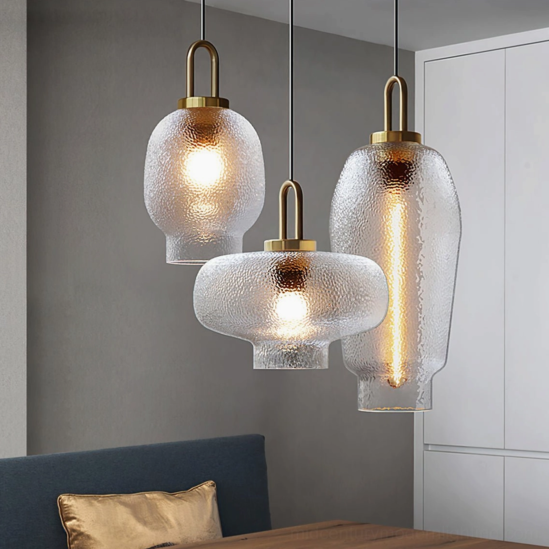Three mixed-shape Marco glass pendant lamps in lounge dining area with navy bench seating and white cabinet