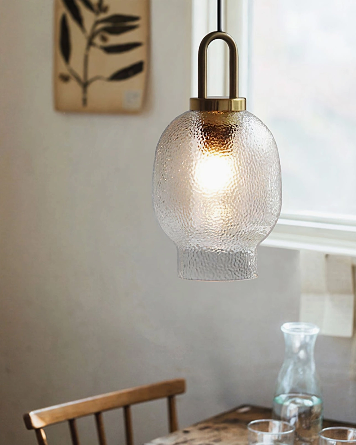 Short barrel Marco pendant lamp suspended over home dining table with wall art and wooden dining chair