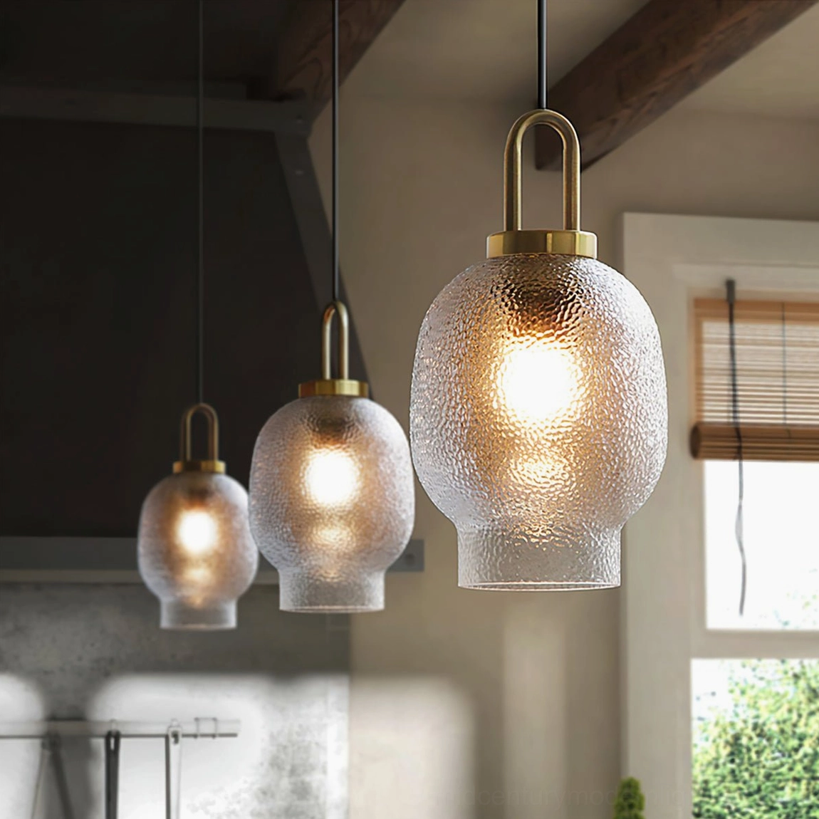 Set of three Marco pendant lamps with mixed sizes suspended over kitchen dining space, brass metal fixtures
