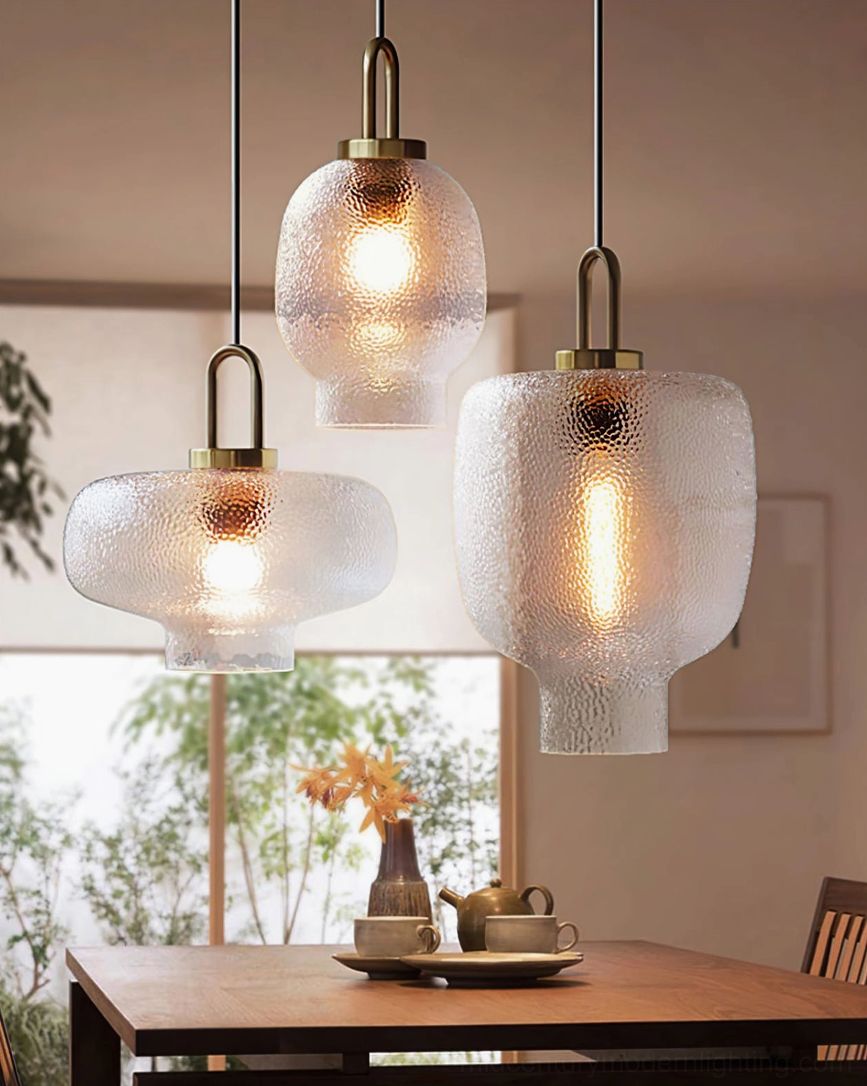 Set of three mixed-size Marco pendant lamps glowing warmly over garden-facing dining area with wooden table