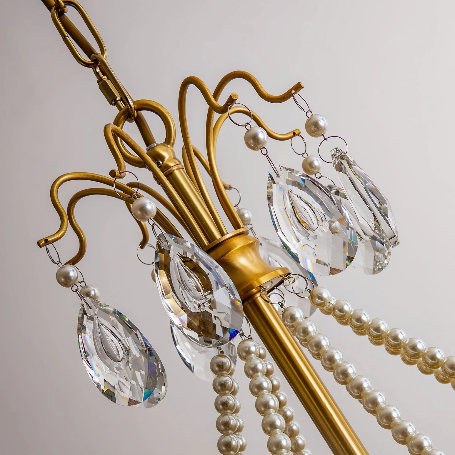 Overhead close-up of Mariposa crystal chandelier showing curved brass frame with crystal and pearl details