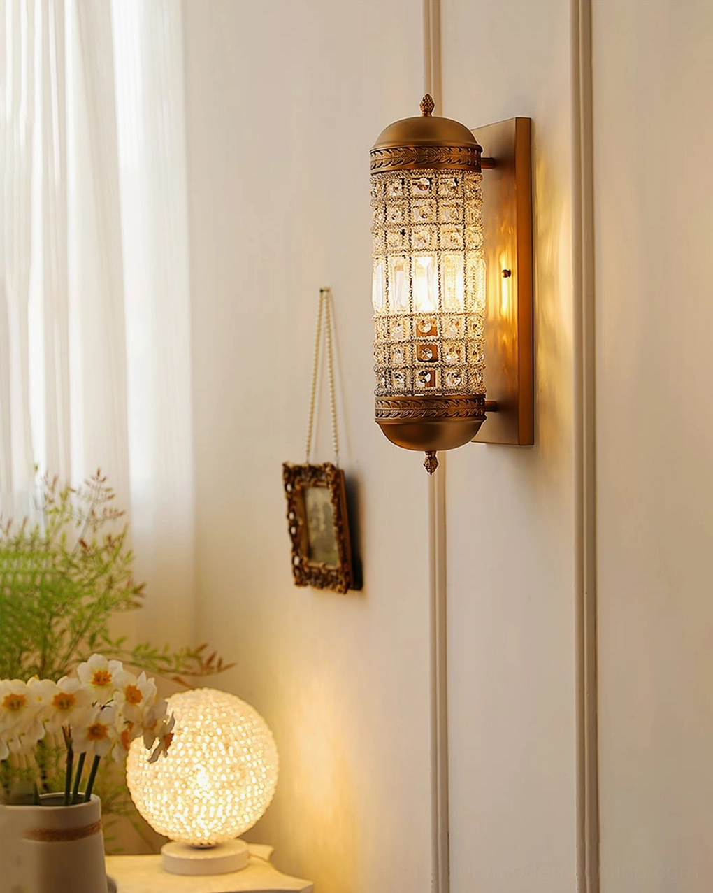 Gold crystal wall lamp installed in bohemian home corner with brass accents and greenery
