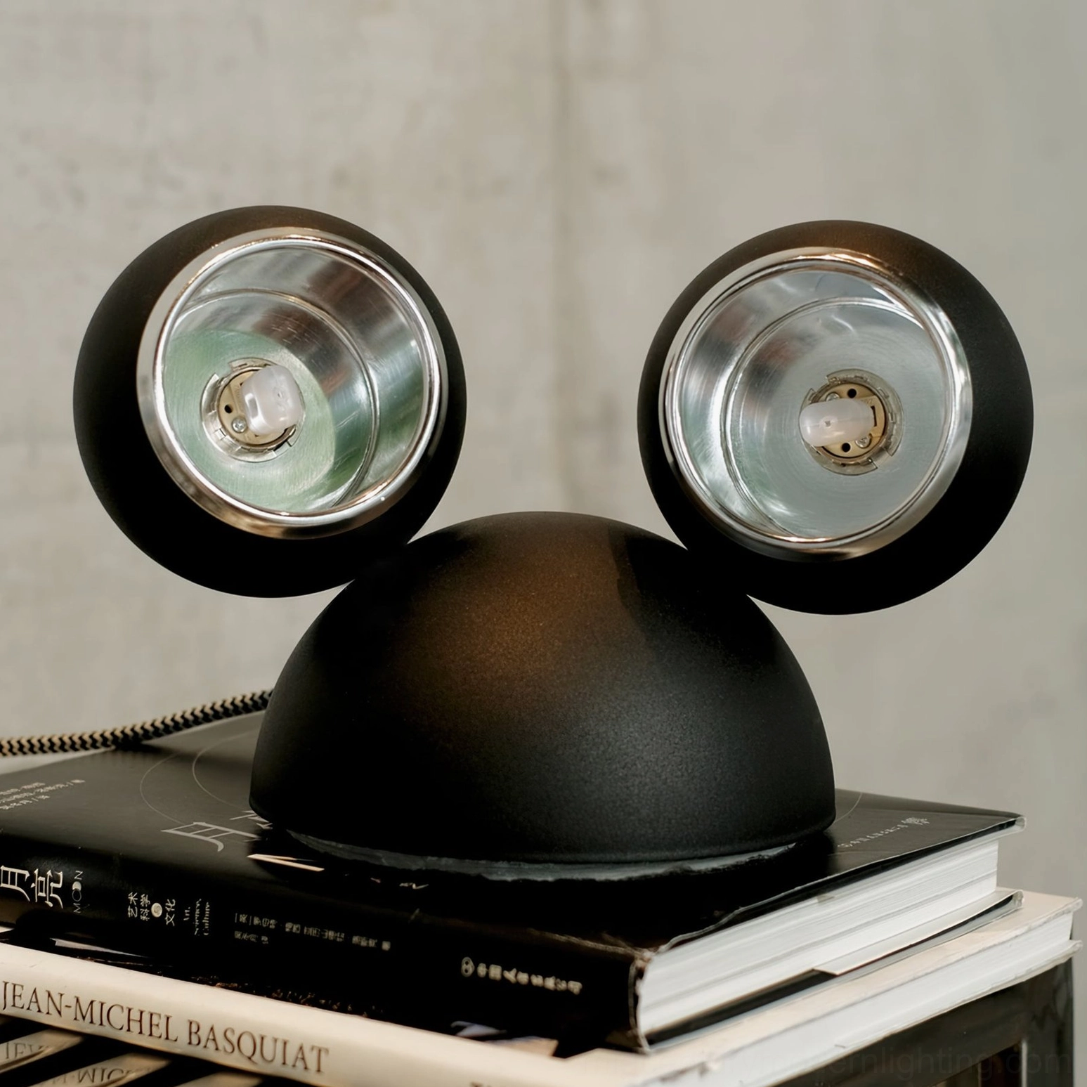 Matte black Mickey table lamp three-quarter front view with stacked art and design books