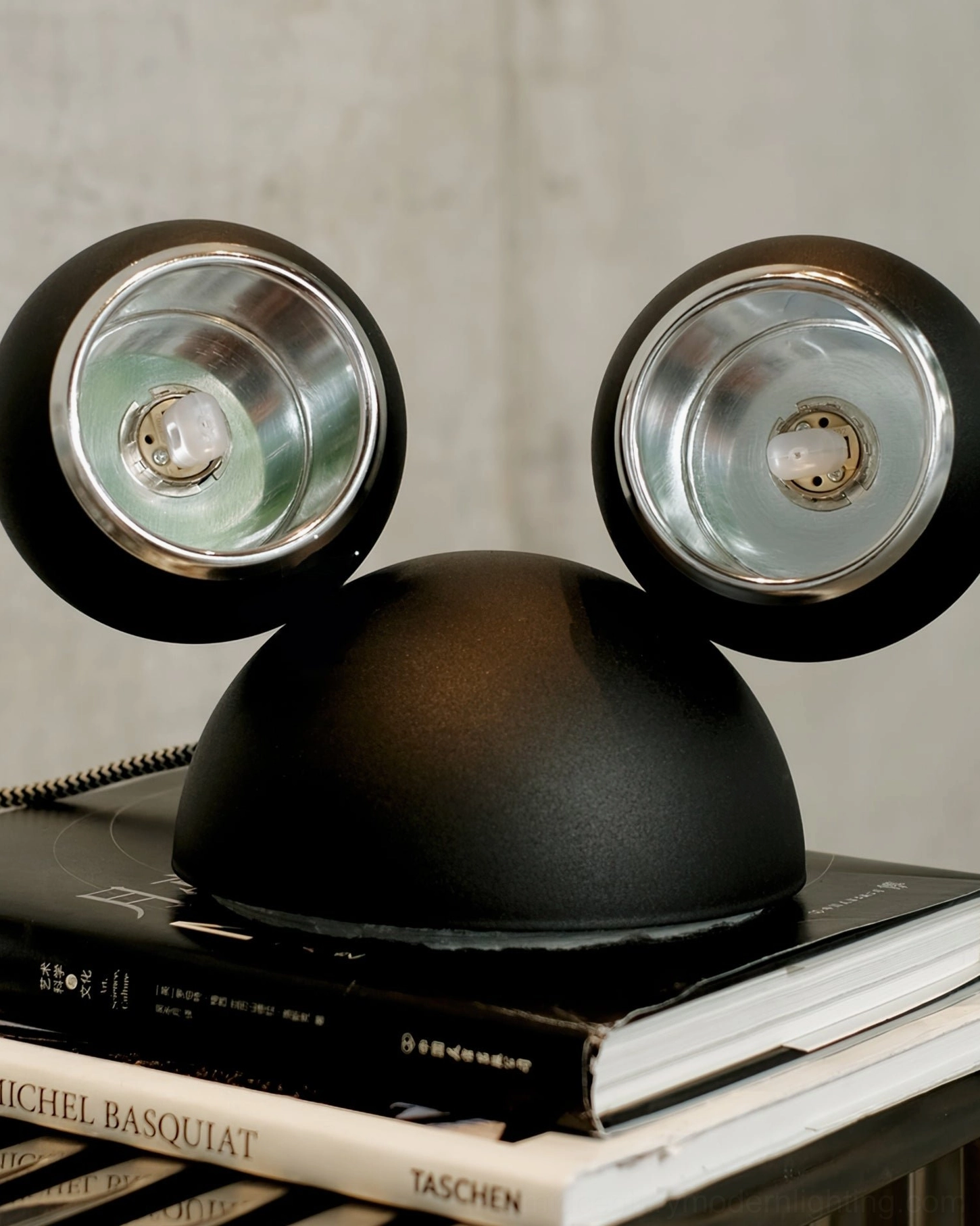 Unlit matte black Mickey table lamp close-up shot on stacked art reference books
