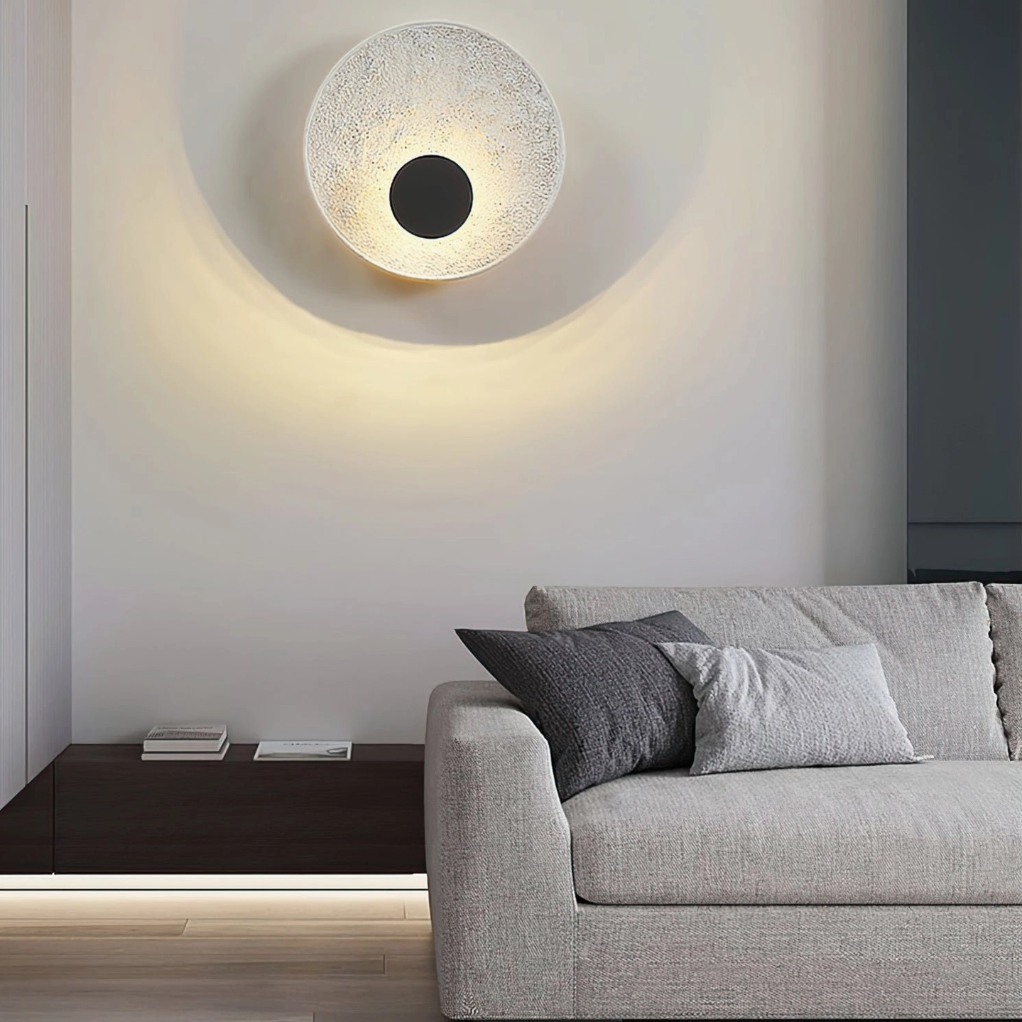 Melesa textured wall lamp in off-white finish with black center displayed above grey sofa in modern living space