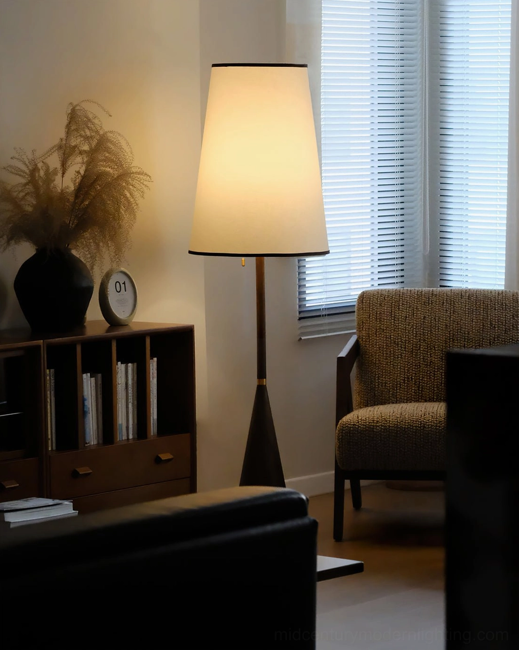 Mezzo floor lamp in cozy reading nook with wooden bookshelf and woven armchair, warm ambient lighting