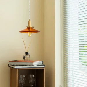 Amber pendant light hanging in cozy residential space with stacked books and reed diffuser - warm ambient lighting in mid-century modern interior design