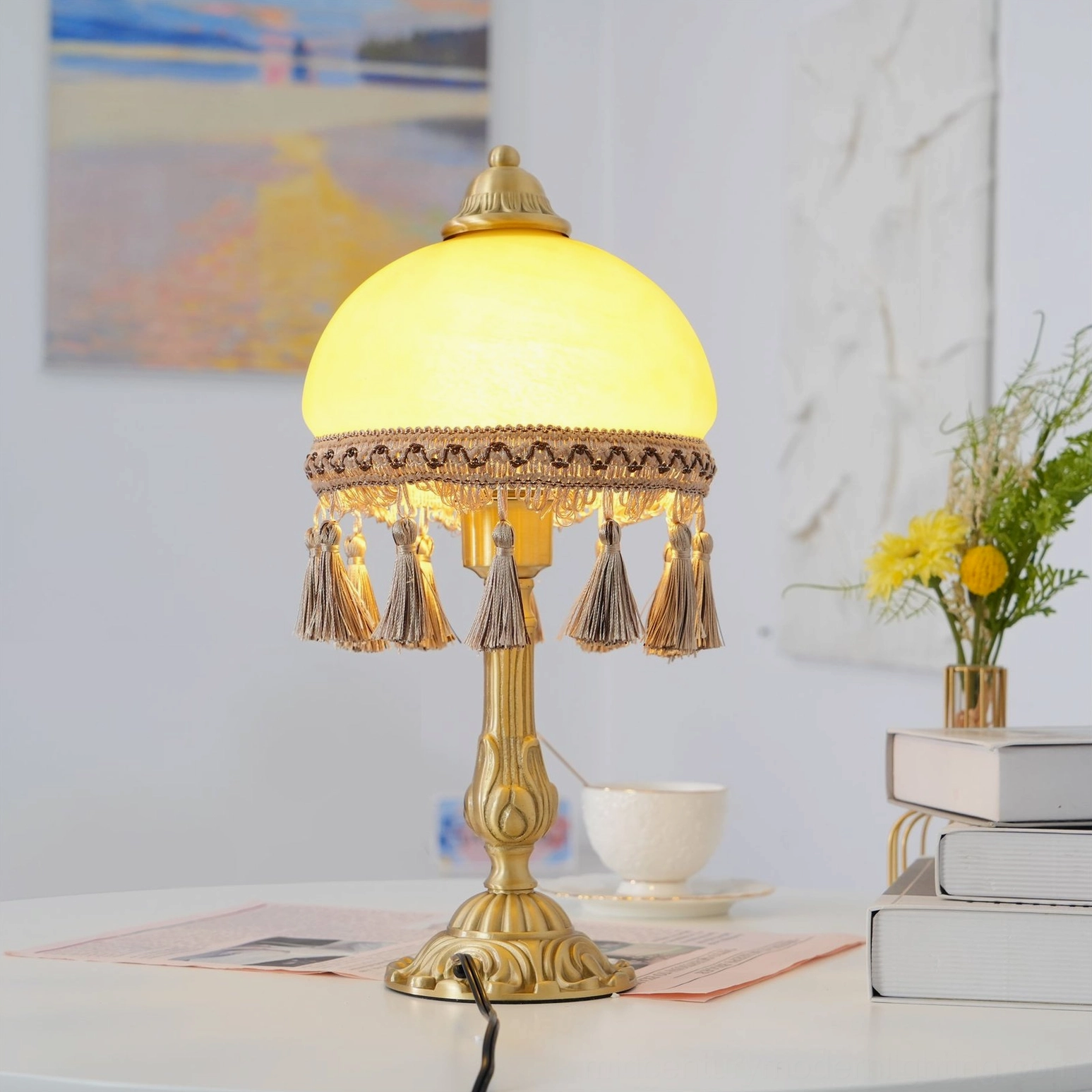 Brass table lamp with beige fabric tassels and embroidered shade trim on minimalist tabletop