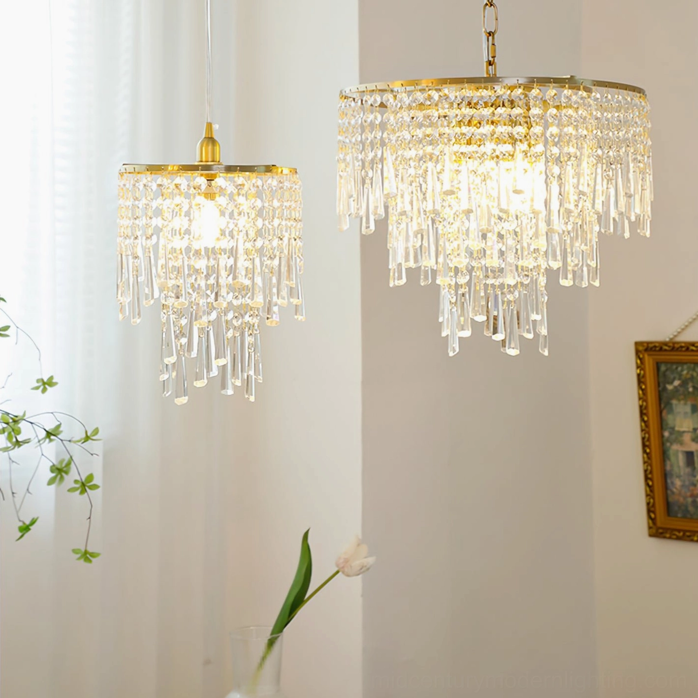 Two matching sizes of cascading crystal pendant lights installed in home interior with green plants and brass gold trim