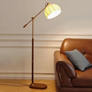 Mid-century modern Anthony floor lamp positioned in living room next to brown leather sofa, demonstrating warm ambient lighting from brass and dark wood pole design