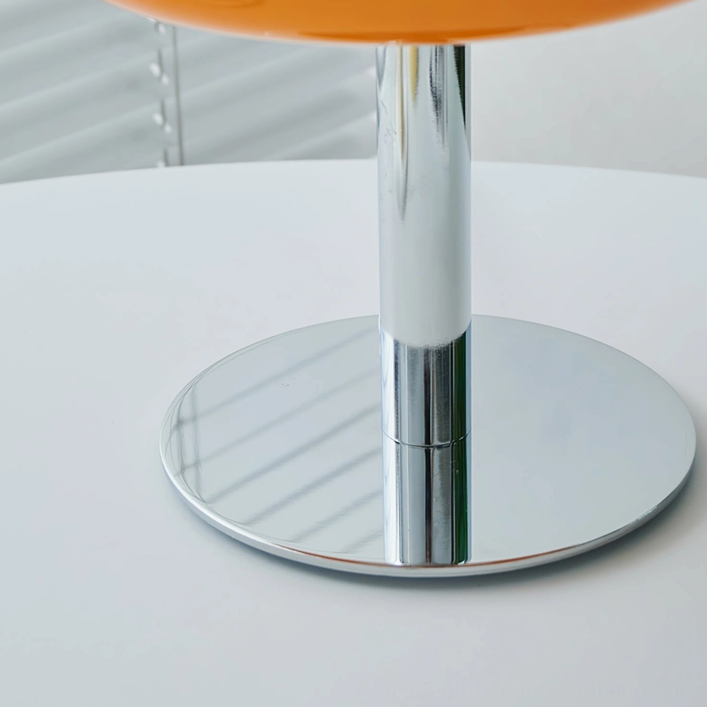 Close-up of polished chrome metal base and stand of mushroom table lamp on white table with blind background