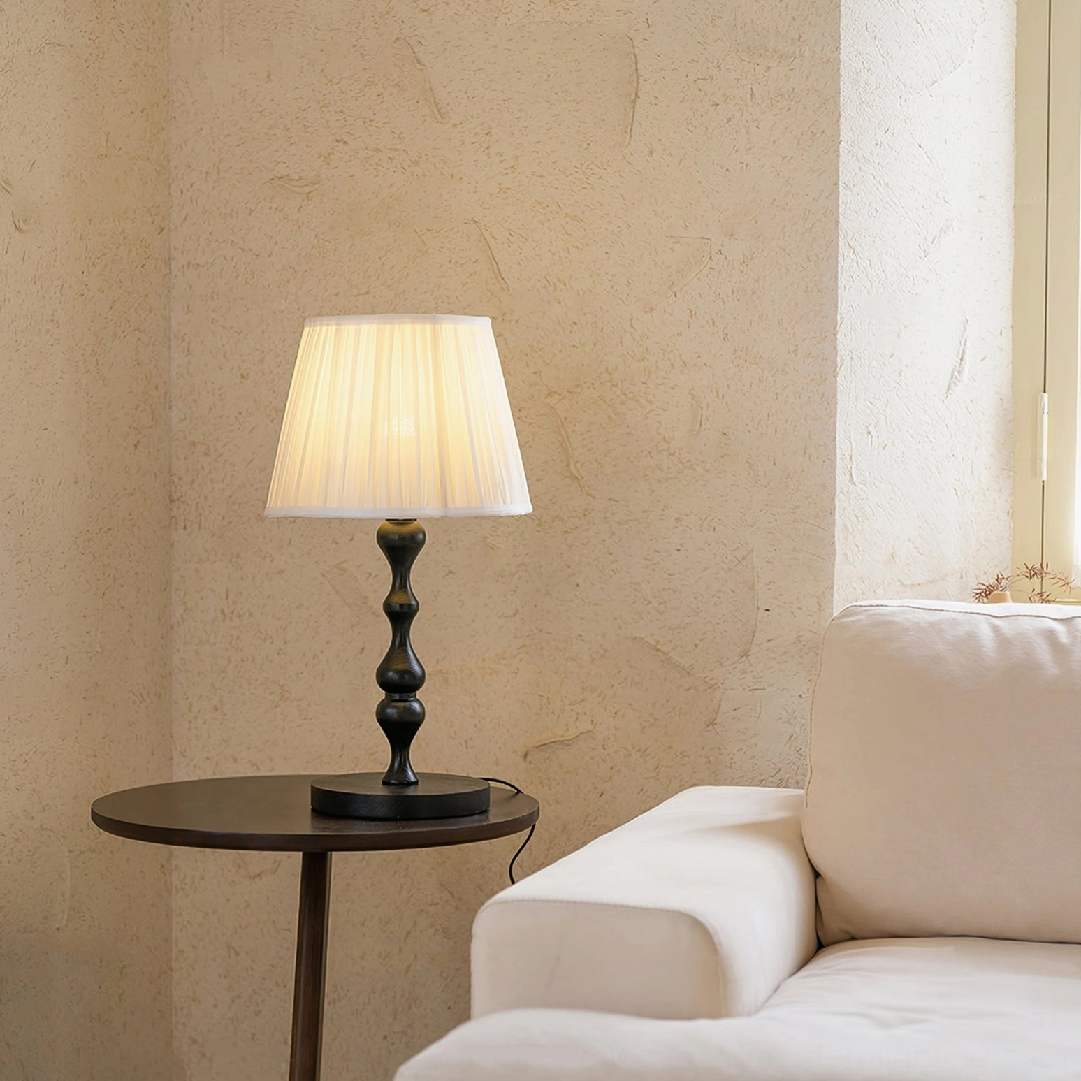 Ambrosia fabric shade table lamp glowing with warm light on side table next to beige sofa, intimate living room ambiance