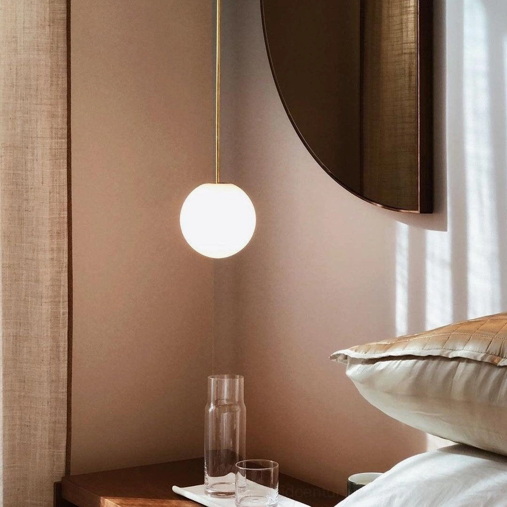 Mid-century modern brass pendant fixture with spherical opal glass in residential setting