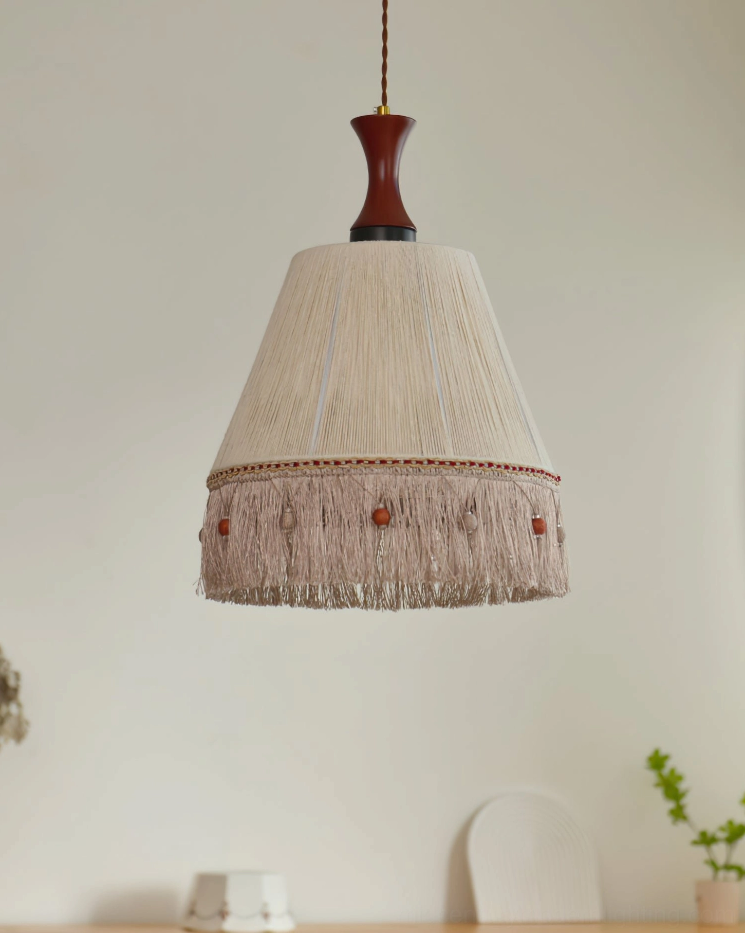 Minimalist beige tassel pendant lamp hanging in corner with potted green plant