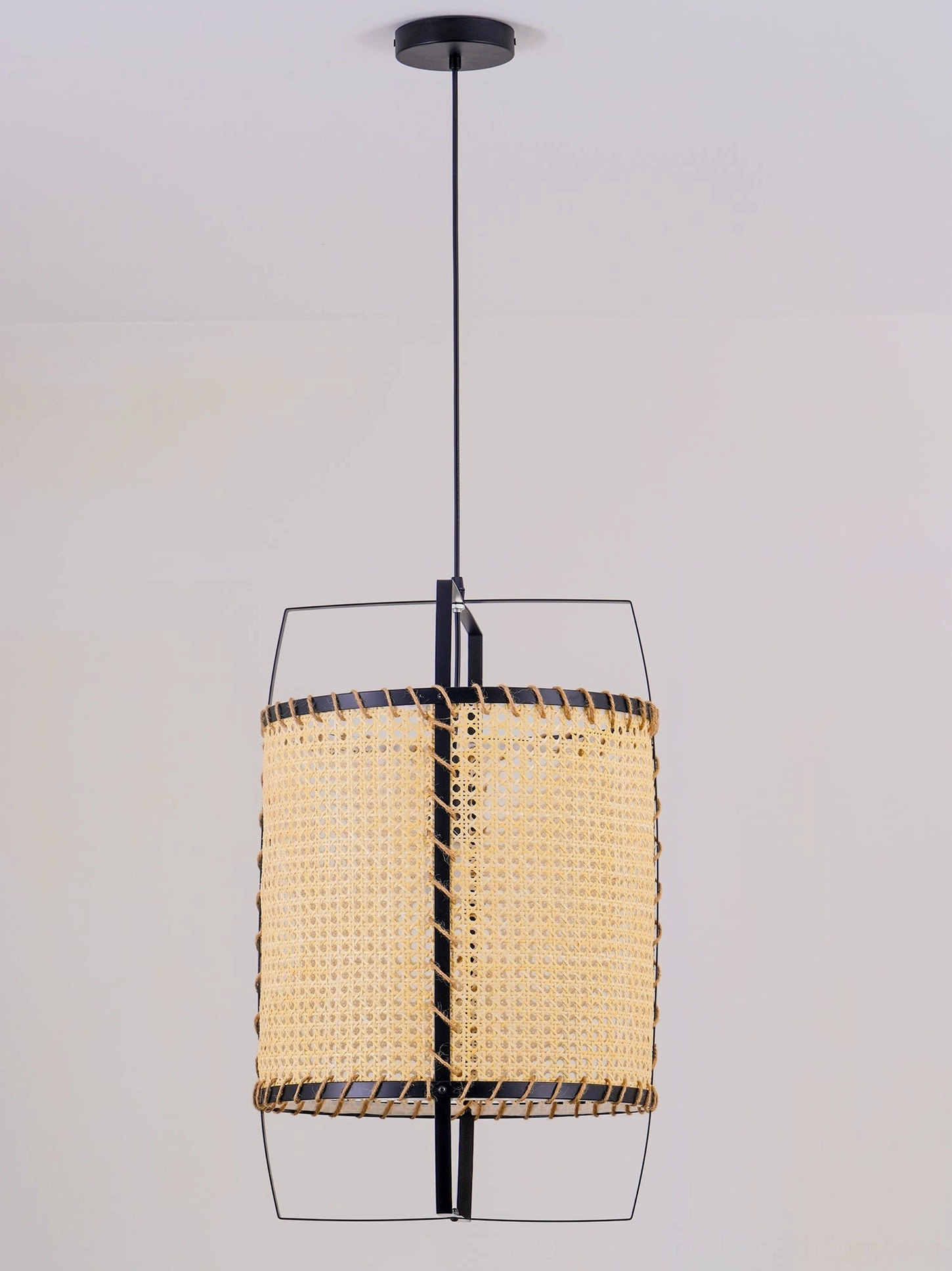Mid-century modern rattan cane pendant light suspended indoors, showcasing geometric open frame design and natural material craftsmanship in bohemian space