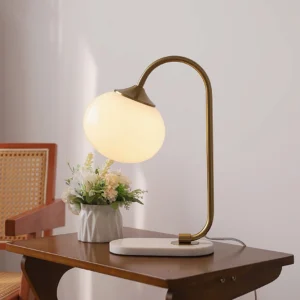 Mid-century modern table lamp with curved brass arm and frosted white glass shade on marble base in home interior setting