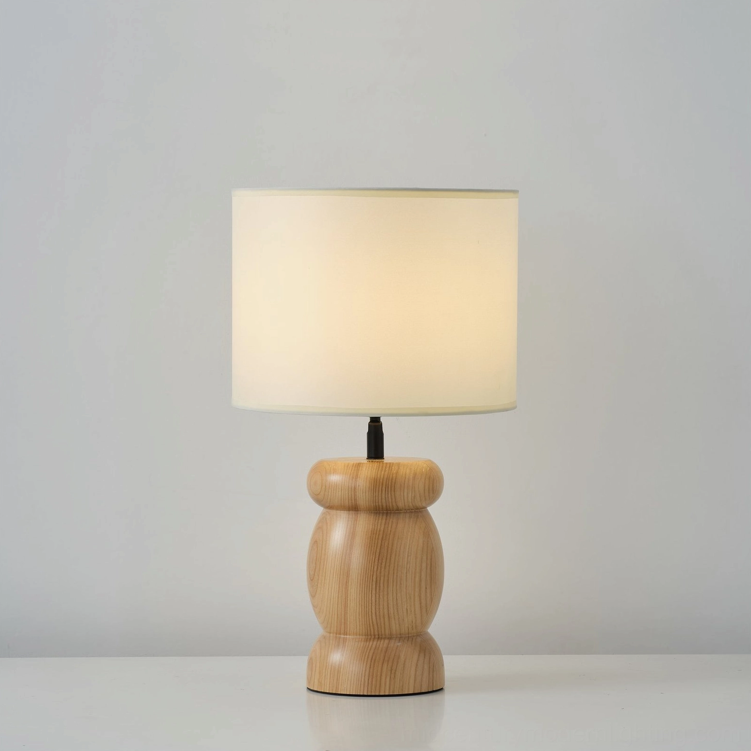 Warm-lit wooden table lamp with fabric diffuser casting soft ambient light, mid-century modern bedside lamp styling