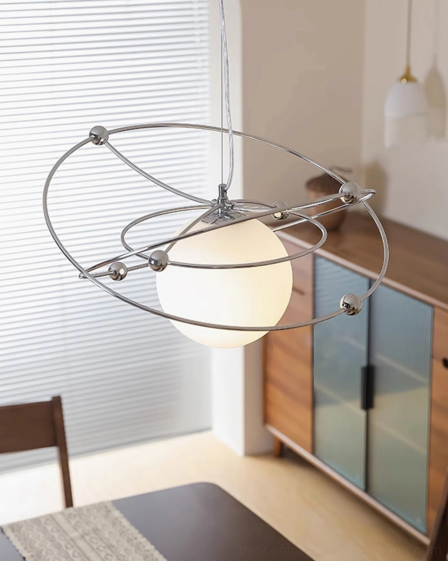 Orbital pendant light illuminating minimalist dining area with wooden furniture and retro decor