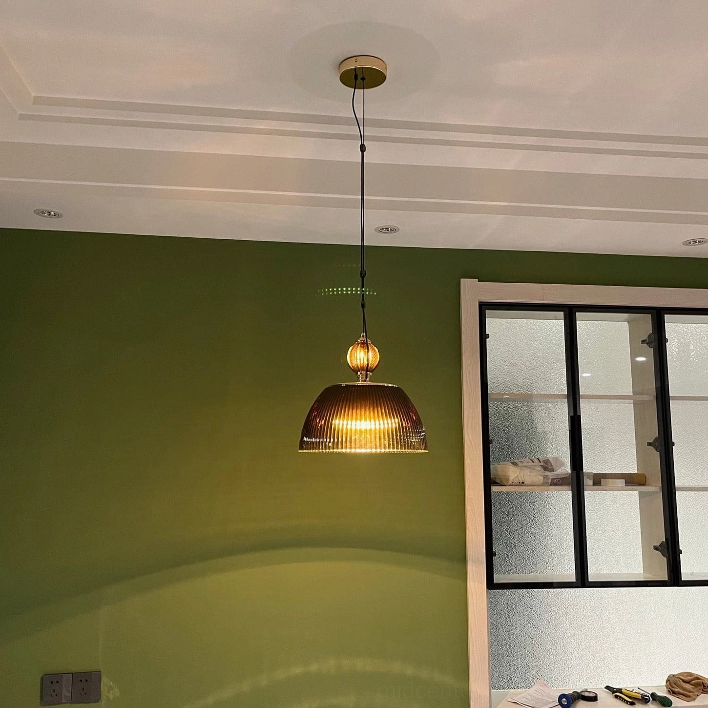 Modern room with mid-century ribbed glass pendant lamp glowing above green accent wall - warm vintage ambient lighting
