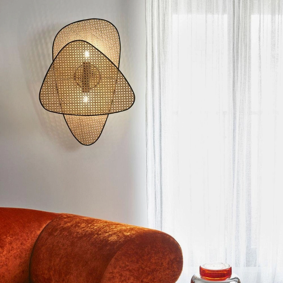 Dual-panel rattan cannage wall lamp in living room with burnt orange velvet sofa and sheer curtains showcasing interior design