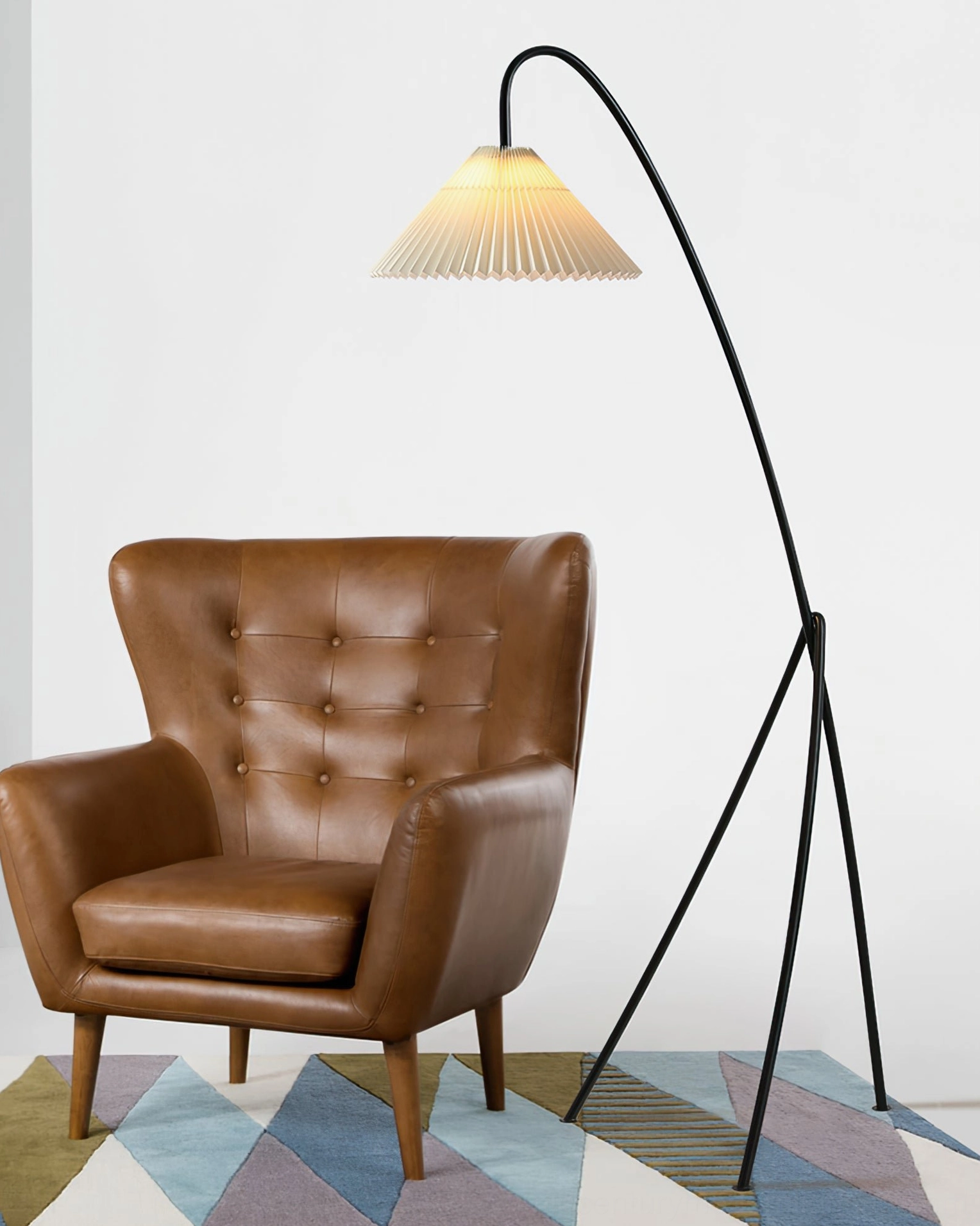 Mid-century modern tripod floor lamp beside tufted leather armchair in living room, three-quarter front view showing warm accent lighting