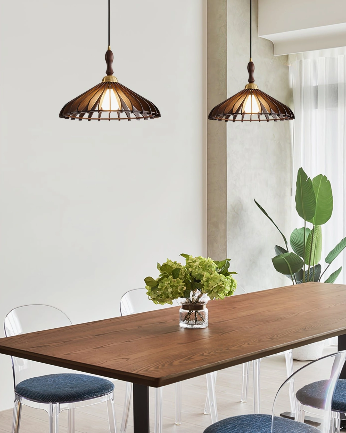 Two dark brown wooden pendant lamps over long wooden dining table with green plant decoration