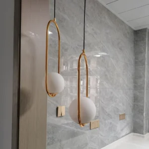Mila oval glass pendant light with brass metal frame mounted on marble wall background, luxury modern interior lighting design