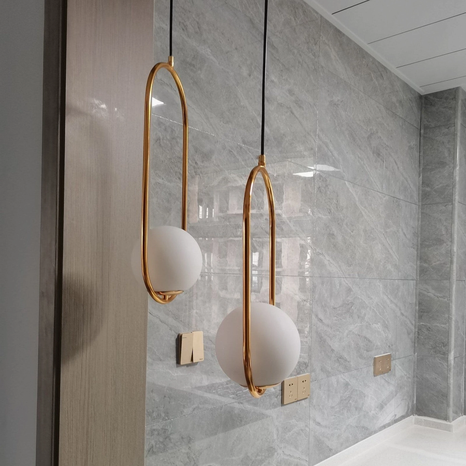 Mila oval glass pendant light with brass metal frame mounted on marble wall background, luxury modern interior lighting design